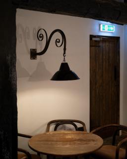 At the back of the pub is a large room that was formerly home to a darts board, a scythe and a cash machine. The plaster was rotten, and sagging sheets of plasterboard adulterated the vaulting of the ceiling. Outdoor paving stones made the room permanently cold and a Hogwarts-style chandelier flickered its orange bulbs above. 

The resulting design is intentionally minimalist. I wanted to expose the original shape of the room and let the lime plaster do the talking. The fire door was re-stained and its architrave removed. This large enamel pendant light, with its scrolled, wrought-iron bracket, helps to fill the space.